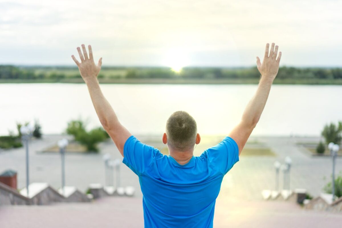 Relaxing view of a man raising arms by the river in Kherson, Ukraine, enjoying the peaceful outdoors.