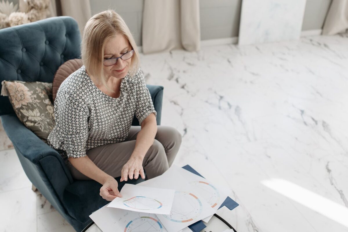 services-07 A woman carefully examines astrological charts while seated in a cozy indoor setting, showing focus and interest.
