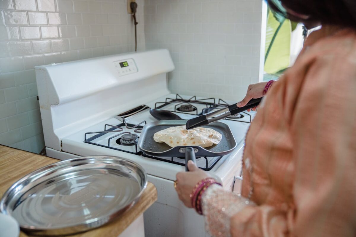A woman preparing traditional flatbread on a stove in a domestic kitchen setting.